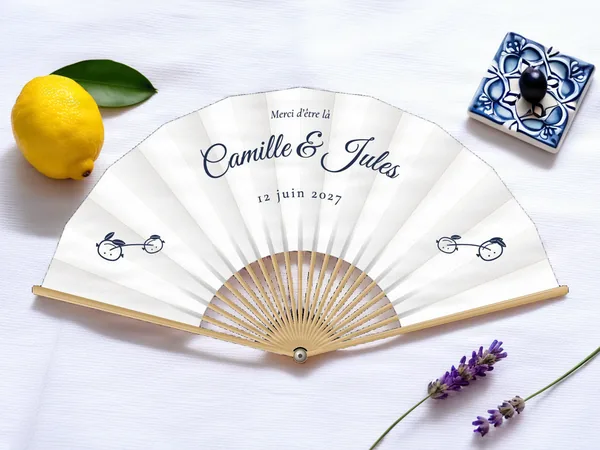 Éventail de mariage personnalisé « Citronnier », petite branche à deux citrons de chaque côté sous les prénoms, toile : blanc, impression : bleu marine, posé sur une table de mariage