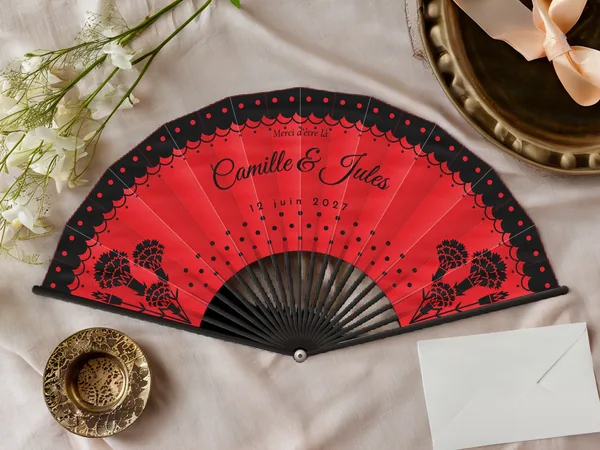 Éventail de mariage personnalisé « Flamenco », volant de dentelle à pois sur le bord et œillets dans les coins, toile : rouge, impression : noir, posé sur une table de mariage