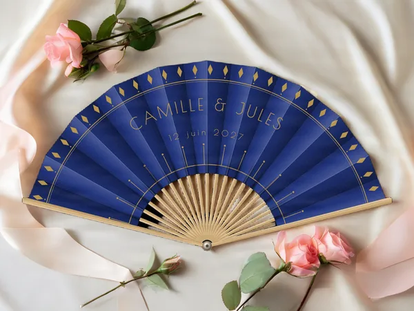 Éventail de mariage personnalisé « Gatsby », losanges le long du bord et rayons Art déco sous les prénoms, toile : bleu marine, impression : or, posé sur une table de mariage