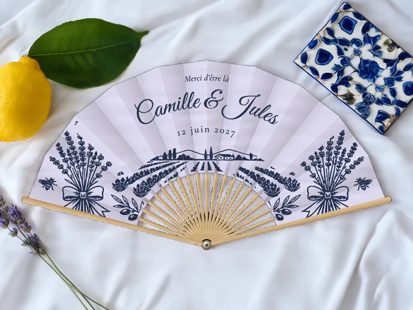 Éventail de mariage personnalisé « Champ de lavande », bouquets de lavande, abeilles et champ de lavande sous les prénoms, toile : lavande, impression : bleu marine, posé sur une table de mariage