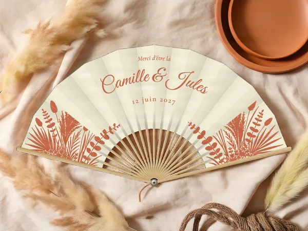 Éventail de mariage personnalisé « Herbes de la pampa », herbes de pampa, palmes et feuillages séchés dans les coins bas, toile : ivoire, impression : terracotta, posé sur une table de mariage