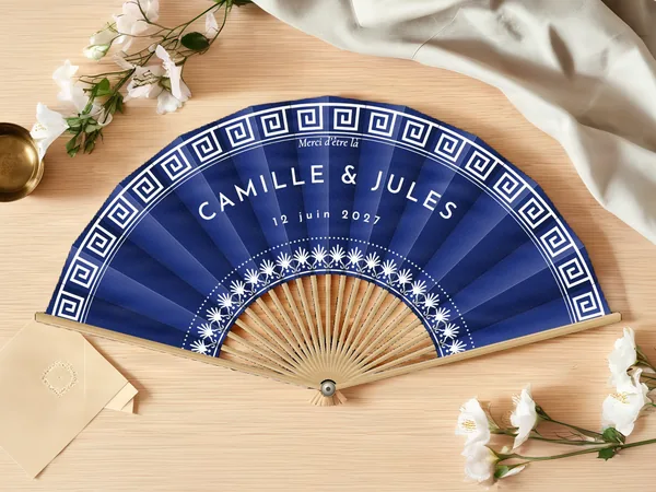 Éventail de mariage personnalisé « Santorin », frise grecque sur le bord et couronne de fleurs autour du centre, toile : bleu marine, impression : blanc, posé sur une table de mariage