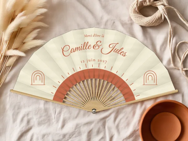 Éventail de mariage personnalisé « Soleil bohème », demi-soleil rayonnant sous les prénoms et petites arches sur les côtés, toile : ivoire, impression : terracotta, posé sur une table de mariage